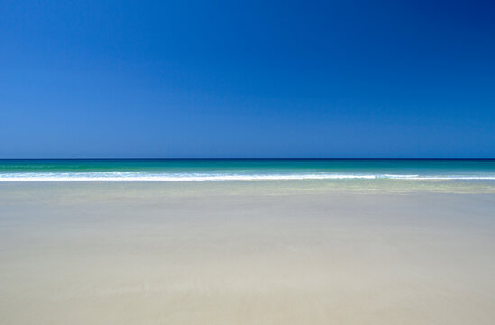 Calm tropical water meets blues sky and pristine sandy beach