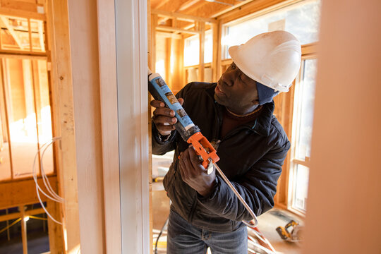 Male construction worker using caulk gun at construction site