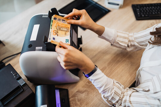 A female worker in an exchange office counts money using counting machine.