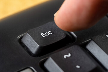 Man pressing the escape key on a simple black office keyboard, finger pushing the esc key button,...