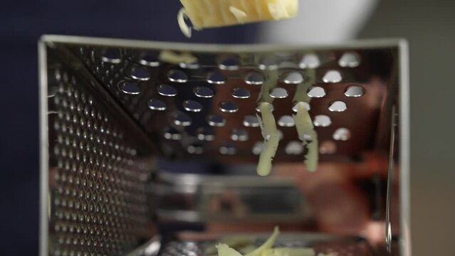 Woman hand rubbing the cheese on metal grater bottom view. home food