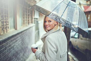 Warming up with a coffee. Rearview portrait of an attractive young woman walking in the rain with...