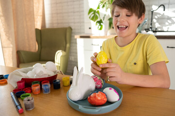 Cute little boy 8 years old painting easter eggs with paint brushes. concept of kid creativity, diy, handmade. paints eggs for Easter holiday. Preparing for celebration is a joy for kids..