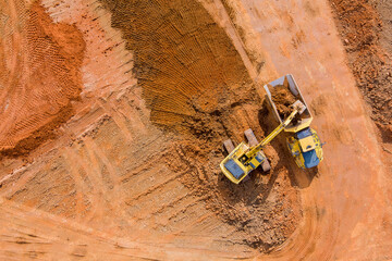 Aerial view of bulldozer is scraping a layer of soil and excavator is digging and dumping earth for...