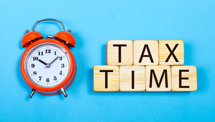 The word tax time is written on wooden cubes with an alarm clock on a blue background. Tax Reminder