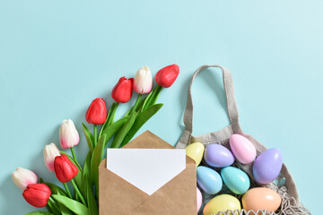 A beautiful bouquet of tulips with a string bag containing painted eggs. Banner for the Happy Easter holiday. Copy space. Flat lay, top view.