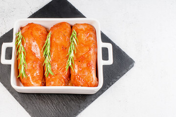 Raw marinated chicken fillet with fresh rosemary.Marinated chicken fillet in red sauce in a plate for roasting in the oven on a light background.
