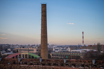 Defunct industrial brick chimney with beautiful cityview in background at sunset. Ecology and industrial renewal concept.