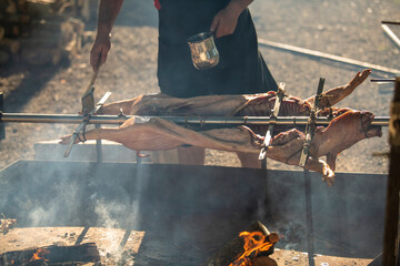 A young suckling pig on a skewer. Whole roasted pig on a rotating steel spit with fire and smoke....