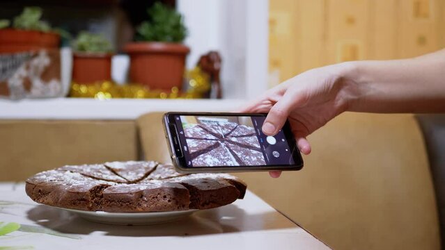 Female Hands Taking a Photo of a Chocolate Pie in Kitchen on a Smart Phone. Blogger takes pictures, a photo review of food on a mobile phone camera. Photographing food. Pressing buttons. Home kitchen.