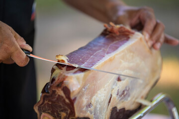Slicing dry-cured ham prosciutto. Professional cutter carving slices from a whole bone, cutting first layer of smoked ham.