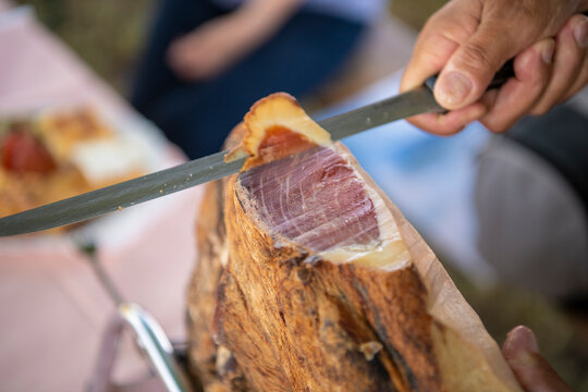 Slicing dry-cured ham prosciutto. Professional cutter carving slices from a whole bone, cutting first layer of smoked ham.