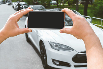 Close-up, Mockup of a smartphone in the hands of a man. Against the background of a white electric car in the city.