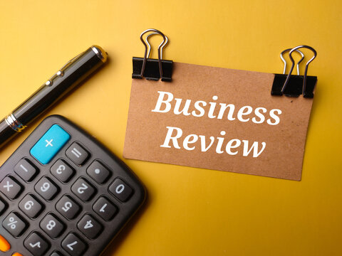 Top view pen,calculator and brown card with text Business Review on yellow background.