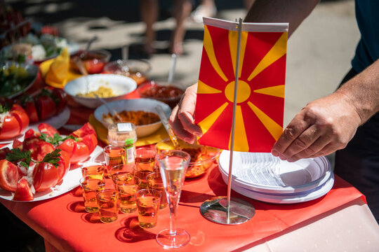 Breakfast buffet with various traditional North Macedonian food and alcohol drinks. Hands holding North Macedonian national flag.