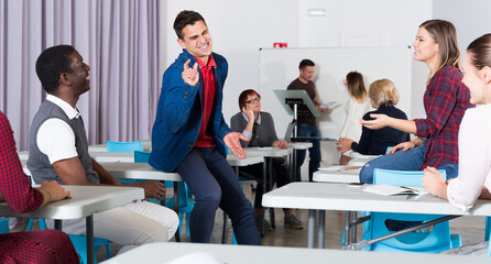 Happy group of adult students lively chatting while enjoying free time in class .