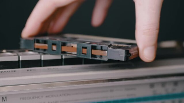Male Hand Takes an an Old Audio Cassette Lying on Buttons of Retro Tape Recorder. Classic vintage, outdated music audio tape cassette from the era of the 80s, 90s. Nostalgia, yearning. Last century.
