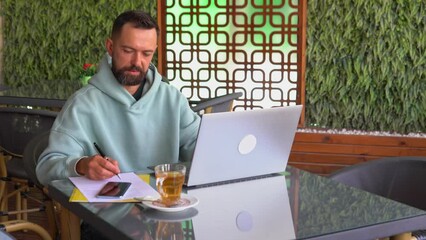 Bearded man with laptop in the cafe writing notes. businessman working anywhere, adult student, study online concept