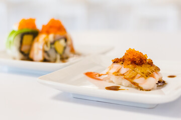 Ebi shrimp cheese sushi topping with tobiko eggs and shoyu soy sauce in front of california rolls sushi.
