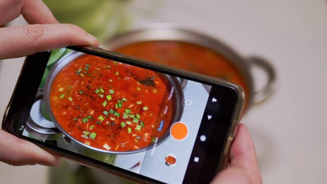 Female Hands are Recording a Video of Traditional Ukrainian Red Borscht on a Smartphone. Photographing food. Video, photo review of food through a mobile phone camera. Home kitchen. Fingerprints.