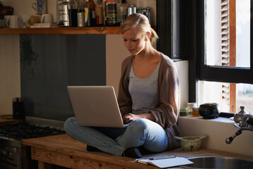 Finding the right recipe online. Shot of a young woman sitting on her kitchen counter using a laptop.