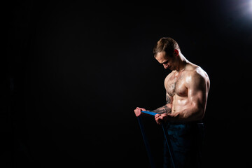 Man on black background keeps dumbbells pumped up in fitness muscle chest torso, athlete fitness dumbbell, shirtless lifestyle. Young sportive metal, one fit With a ribbon in hand, the fitness gum is 