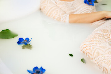 top view of young, sensual woman enjoying milk bath with blue flowers, copy space in center for text