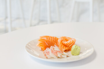 Close up fresh raw salmon and squid slice sashimi with wasabi on  white plate and white table in background, appetizers menu for advertising Japanese restaurants