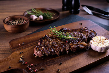 Sliced striploin steak, grillid with 4seasons pepper garlic cloves rosemary ,on stone plate dark and wooden