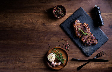 Sliced striploin steak, grillid with 4seasons pepper garlic rosemary, on stone plate dark and wooden background , knife and fork black, top view