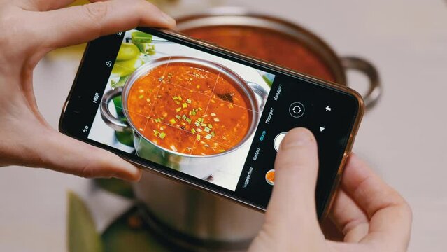 Female Hands Taking a Photo on a Smart phone Traditional Ukrainian Red Borscht. Blogger shoots a picture, a photo review of food on a mobile phone camera. Photographing food. Home kitchen.
