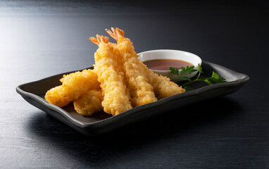 Shrimp tempura on a plate placed against a black background.