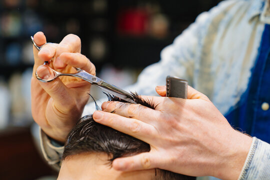 hairdresser makes a haircut for a brunet man with a scissors in a barbershop