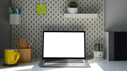 Front view laptop computer, coffee cup and supplies on white table in bright living room.
