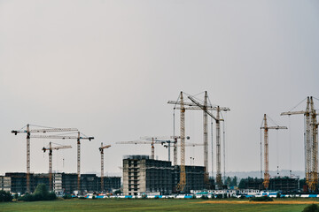 Building site background with copy space. Industrial construction cranes on background of foggy sky. Hoisting cranes and multi-storey buildings of new city districts. Project of urban area.