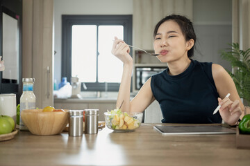 Beautiful asian woman eating fresh vegetable salad at home kitchen. Health care and wellness concept.