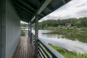 Wooden porch on the bank of the river. Middle lane, cloudy sky, calm summer weather.