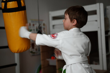 little boy in kimono and helmet training at home punching a punchbag