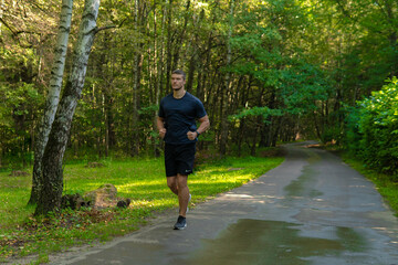 A man athlete runs in the park outdoors, around the forest, oak trees green enduring athletic athlete sport lifestyle trail training wellness park wellbeing. cross, morning stretches
