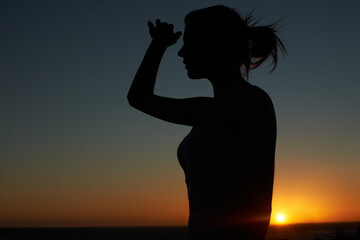 As far as the eye can see. Silhouette of a young woman looking into the distance against a setting sun.