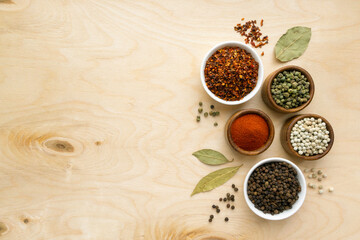 Different types of peppers in small bowls on wooden background, space for text