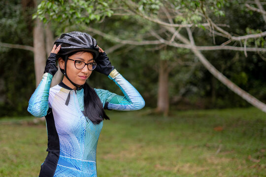 Latin young woman on a bicycle practicing cycling in the forest. Helmet placement, safety.