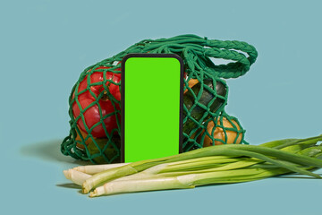Online shopping. A smartphone with a green screen and vegetables in a mesh bag