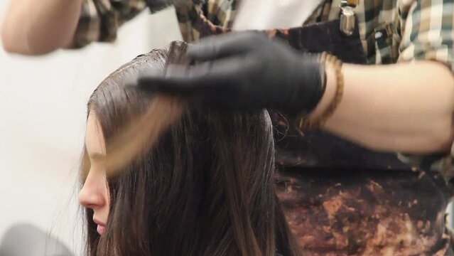 Woman's hair is sectioned and root colour is brushed on by stylist