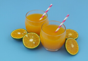 Fresh orange juice with drink straws and green orange fruits slices on blue background	