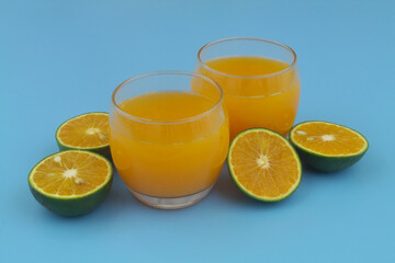 Glasses of fresh orange juice and green orange fruits on blue background	