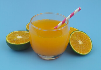Glass of fresh orange juice with drink straw and green orange fruits on blue background	