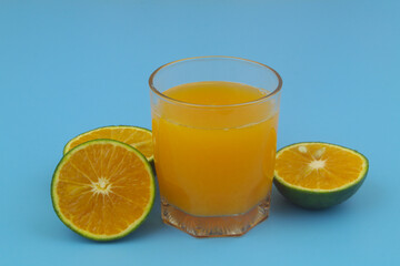 Glass of fresh orange juice and orange fruit slices on blue background	