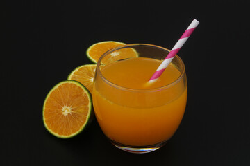 Fresh orange juice with drink straw and orange fruits slices on black background	