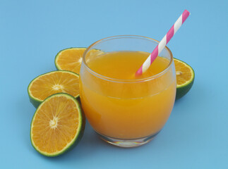 Glass of fresh orange juice with drink straw and green orange fruits on blue background	